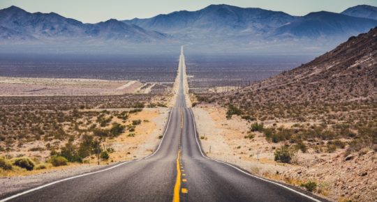 Classic panorama view of an endless straight road running through the barren scenery of the American Southwest with extreme heat haze on a beautiful hot sunny day with blue sky in summer