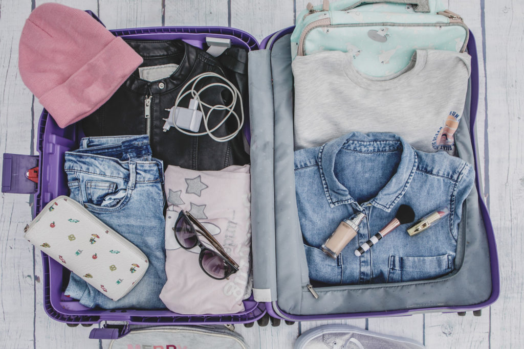 Open suitcase with clothes folded, sunglasses and a charger