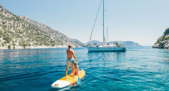 Young couple paddling on stand up paddleboards against the yacht in the sea