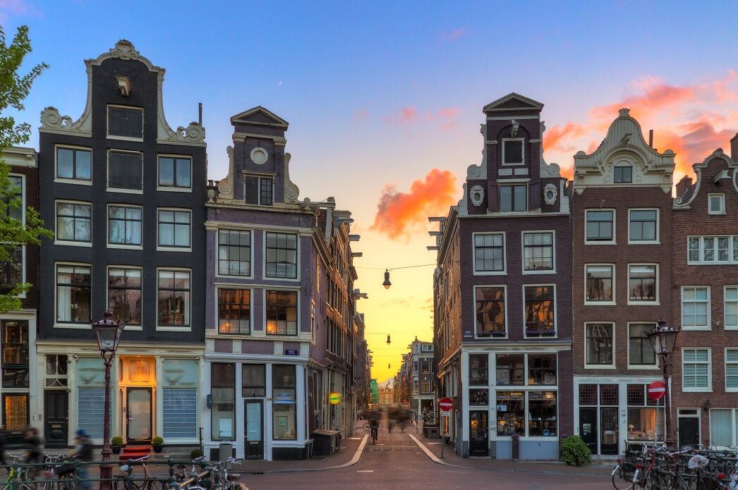 Tall, thin residential houses of Amsterdam with a setting sun in the background.