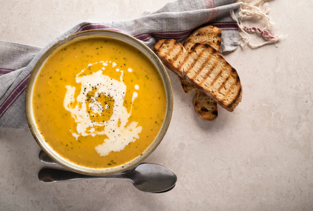Bowl of soup with toasted bread and spoons next to it