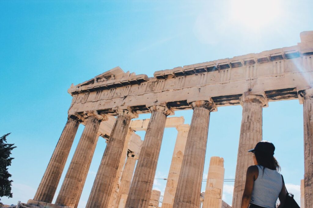 Part of the Acropolis in Athens, with a blue sky in the background and a woman in the foreground.