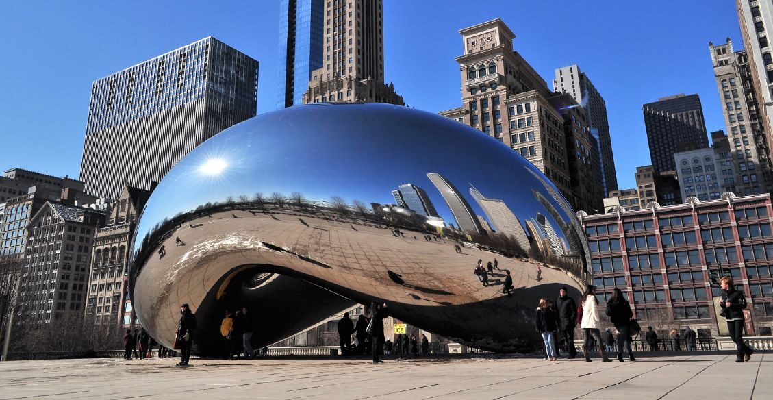 Shining metal sculpture with a backdrop of blue sky and skyscrapers