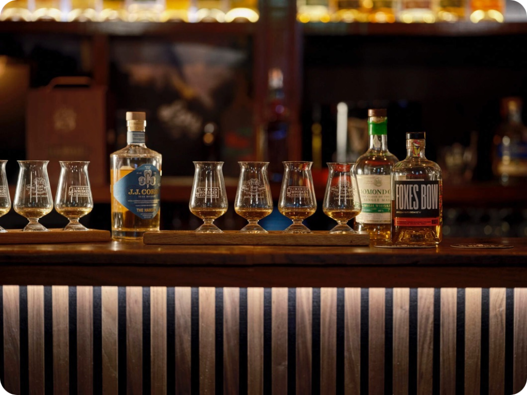 A line up of whiskey tasting glasses and bottles on a bar.