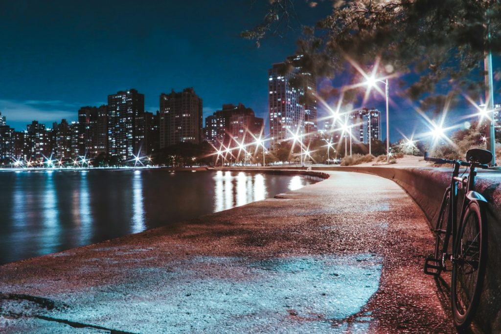 View of a city skyline at night from a trail, with streetlights in the background and a bike parked to the right.