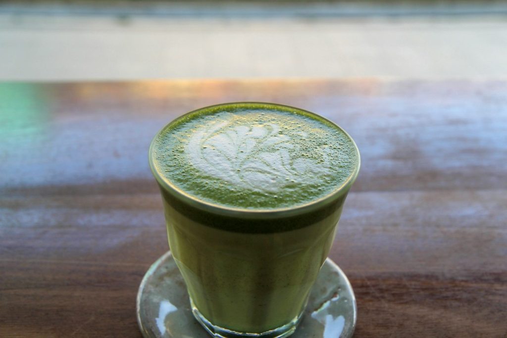 Green matcha latte in a glass cup on wooden table