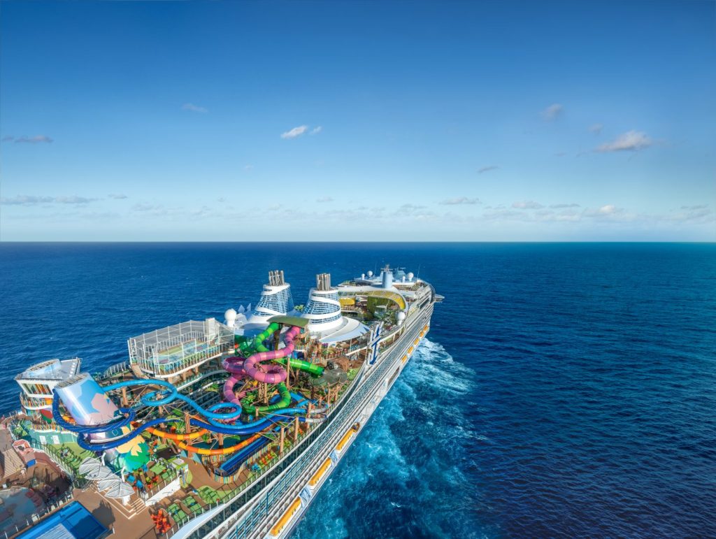 Aerial view of an incredible cruise ship, with theme park, lights, pool and a variety of attractions on top deck. Blue sea surrounds the vessel