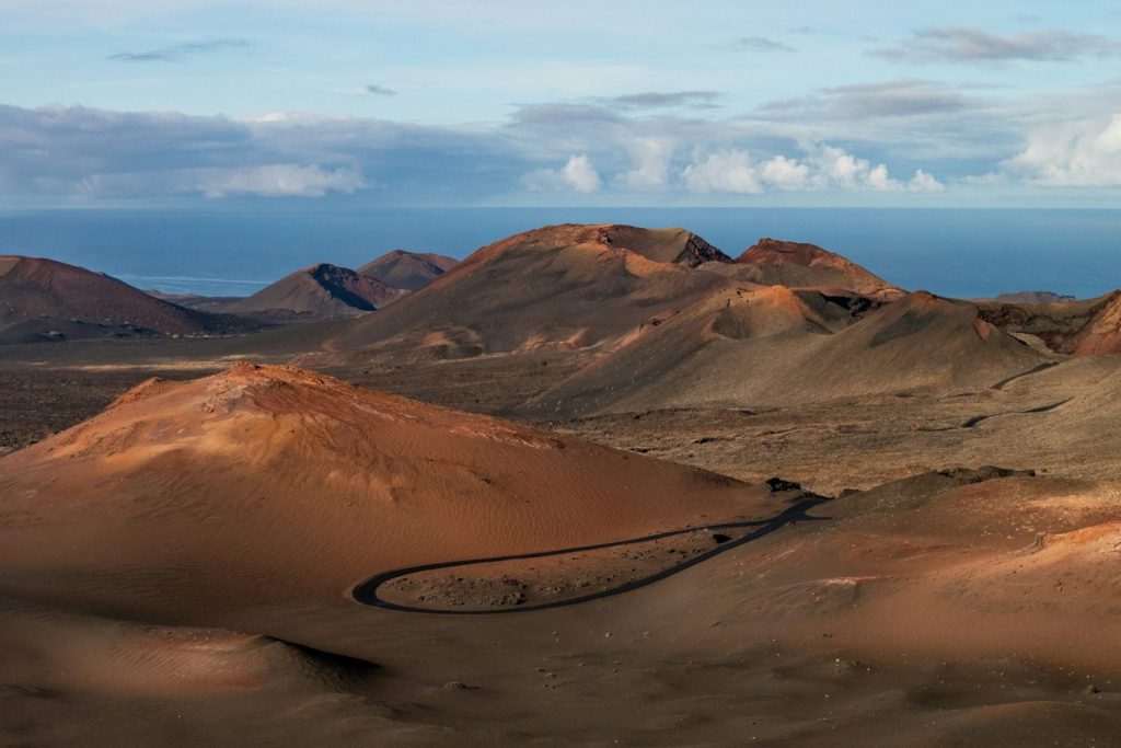 A dirt road winding through a barren, sandy, desert landscape, with clouds in the distance