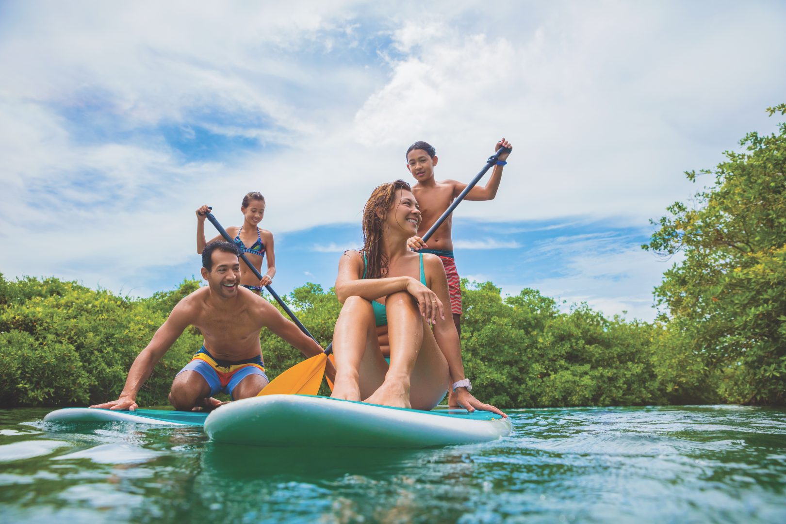 Mother, father and two children paddle boarding on blue waters, with blue sky in background