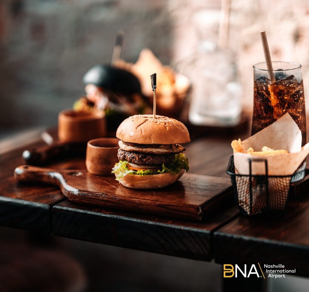 A carefully presented burger, chips and other morself on a dark brown wood platter