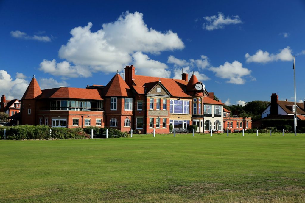 Image of club house with red slate roof, lawn in foreground and blue sky in background