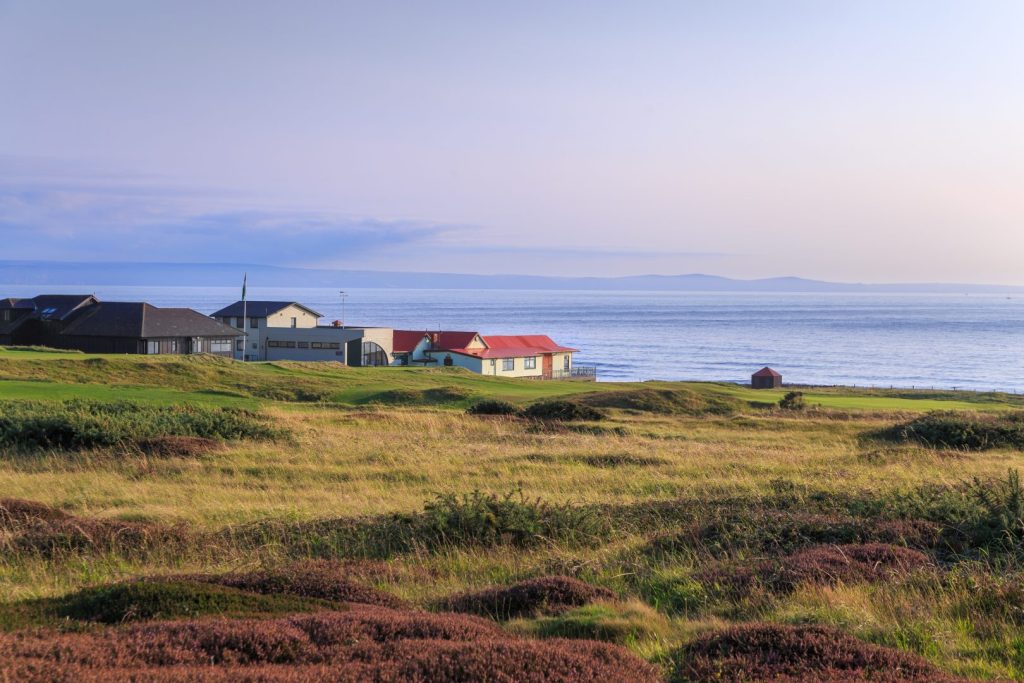 Image of a small house perched between green and gold landscape, sea and sky