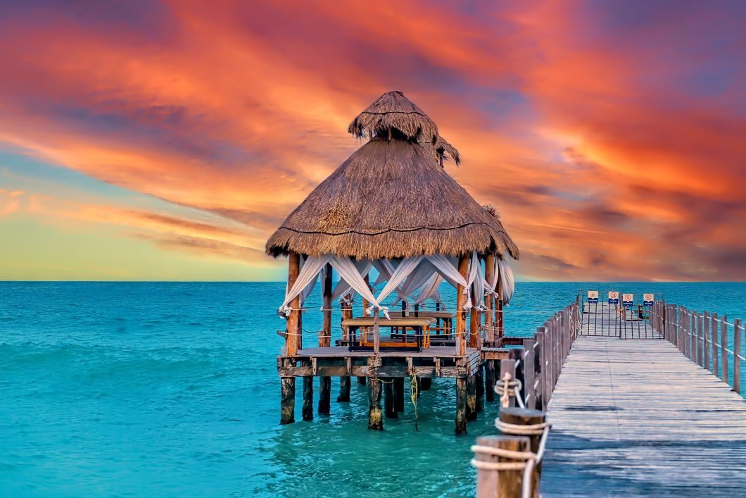 wooden gazebo with a thatched roof, situated at the end of a pier over turquoise water in Cancun