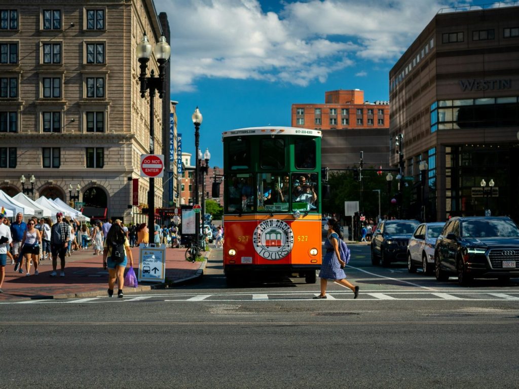 A streetcar on a city street with market stalls and buildings in the background.