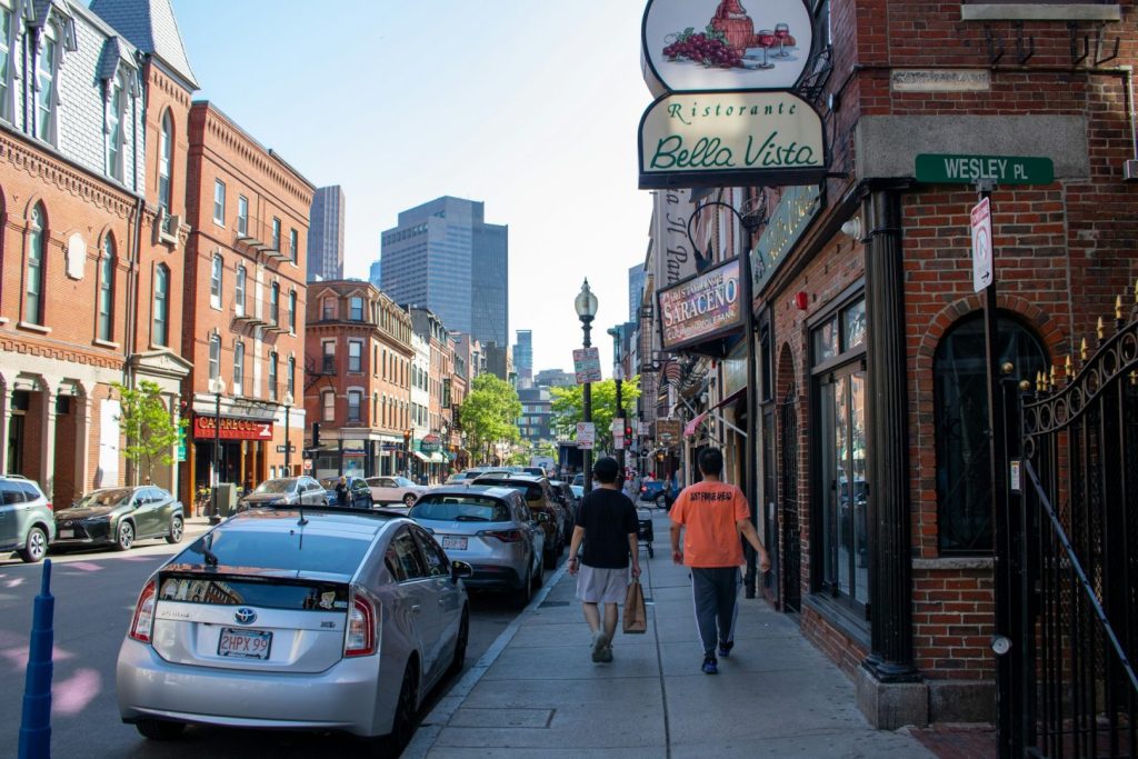 Two people walking along a city street with cars and buildings on either side.
