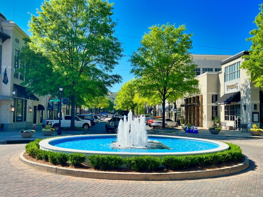 A water fountain in a town square with buildings and blue sky behind