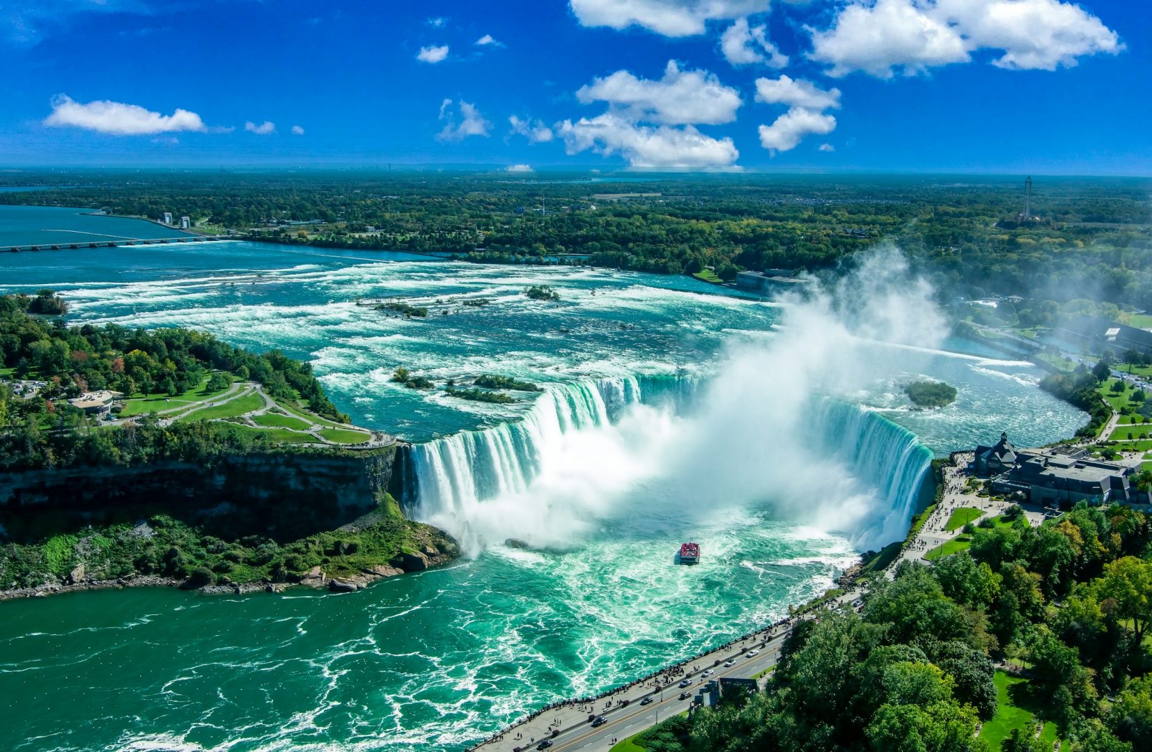 Aerial view of waterfall and surrounding lake, cliffs and land, with blue sky above