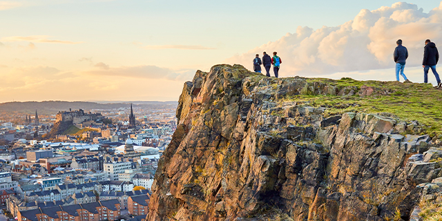 Group of people walking along cliff edge at Salisbury Crags, Holyrood Park with Edinburgh city the in background at sunset