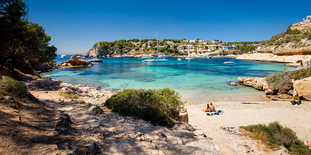 Couple sitting on beach cove looking out at yachts in Mallorca, Spain